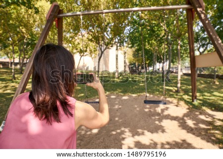 view of a woman photographing some swings with her mobile