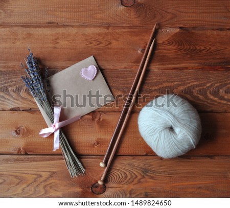Bouquet of lavender with a pink ribbon and craft envelope, knitting needles with a heart and one woolen clew on a wooden background