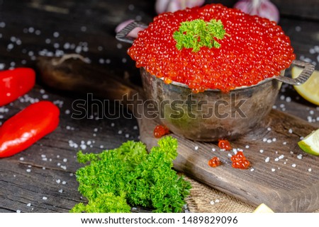 Large red caviar in rustic vintage style, a deep bowl of buckets saucepan, on a wooden cutting board and table, with greens, vegetables, lemon and lime, large sea salt, dark light, top side to bottom
