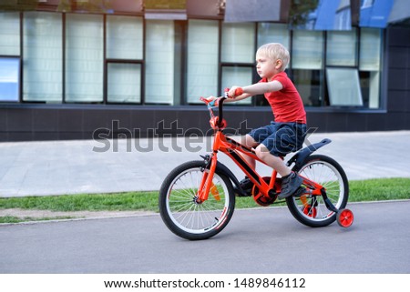 Handsome blond boy rides on a children's bicycle. Urban background