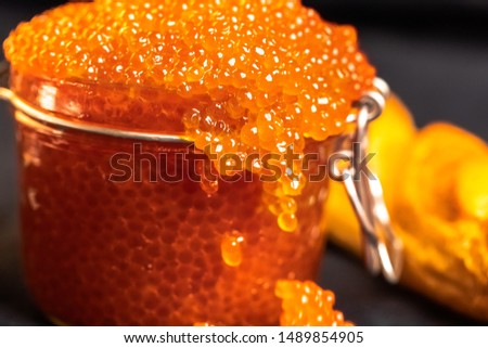 large red caviar in a jar, pick up with a spoon, lies on parchment, next to a loaf of bread a baguette, lie on a gray background with a piece of cloth