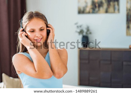portrait of young teenager brunette girl with long hair in blue dress listening music on headphones in room