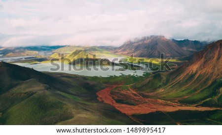 Beautiful Icelandic landscape of highlands with orange and yellow colorful mountains and hills, lake and rivers green moss fields and grey cloudy sky on the background in national park Landmannalaugar