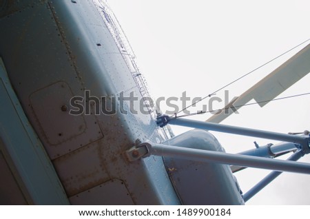 In the photo of the gray and blue helicopter-wing, cabin, tail, propeller, chassis. In the background, a bright sky with clouds.