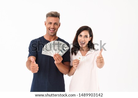 Picture of optimistic adult loving couple isolated over white wall background holding money and credit card showing thumbs up.