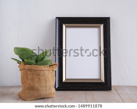 Black photo frame with tree over white wall.