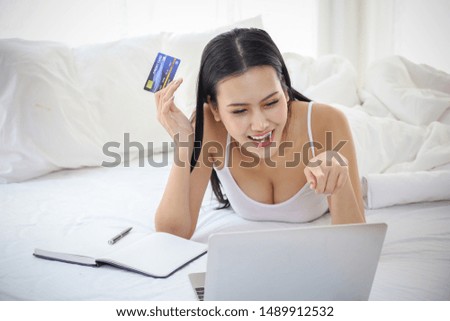 A Asian beautiful woman is on bed and using credit card for shopping online in website by laptop computer, e-commerce or marketing or internet of thing, technology network or modern lifestyle concept