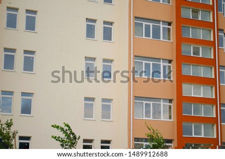 Multi-storey house with beige and red, orange walls, Windows and green trees.