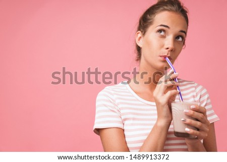 Image closeup of young gorgeous woman smiling and drinking chocolate milk with straw isolated over pink background