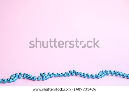Artificial blue beads in a line on a pink background. Festive background, new year. Copyspace.
