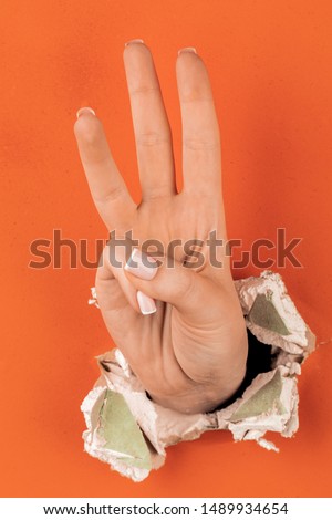 women's hand shows gesture through broken orange drywall
