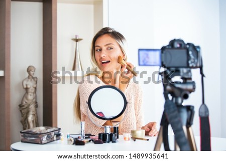 Famous blogger. Cheerful female vlogger is showing cosmetics products while recording video and giving advices for her beauty blog. Focus on digital camera