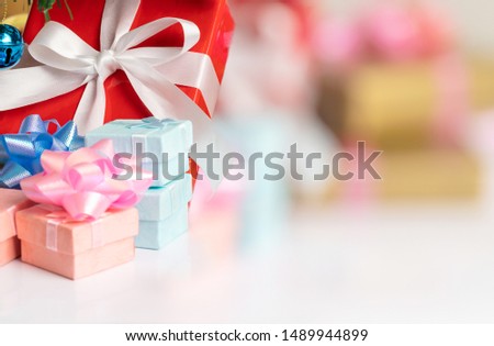 Close up a red gift box tied with a white ribbon placed on the table including a small, colorful box placed under the Christmas tree. There is room for text input. Select focus shallow depth of field.