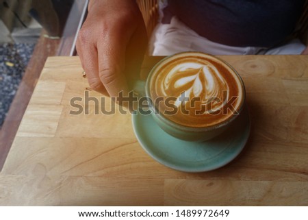 Man holding green cup of hot latte coffee  by hand on wooden table with sunlight.                                
