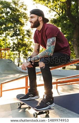 Attractive cheerful young man sitting at the skate park ramp with a skateboard