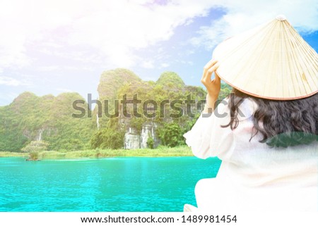 Clove up Asian  woman tourist is wearing Vietnamese Hat (Non La) and traveling sitting on boath looking mountain and sky views. Image is extremely overexposed.                             