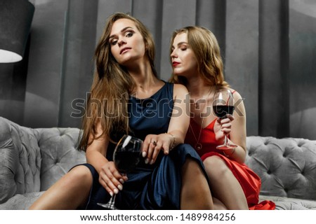 beautiful girls in dresses on the couch; glasses of wine in hand
