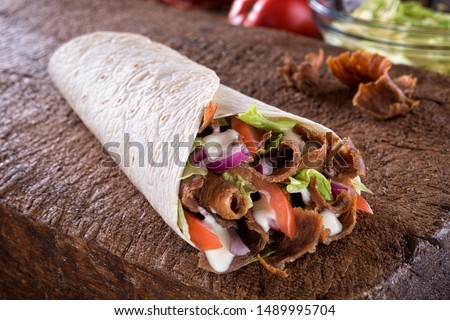A delicious doner donair kebab wrap with spicy meat, lettuce, tomato, red onion and sauce. Royalty-Free Stock Photo #1489995704
