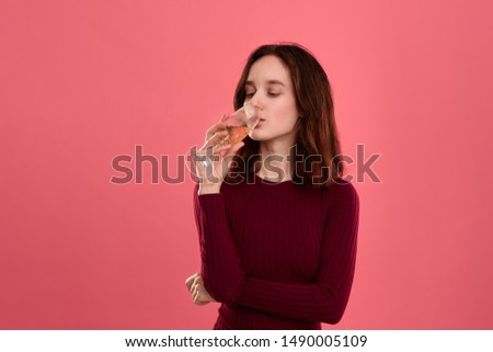 Excited pretty brunette girl drinking sparkling champagne from a wineglass standing isolated on a dark pink background. Concept of celebration