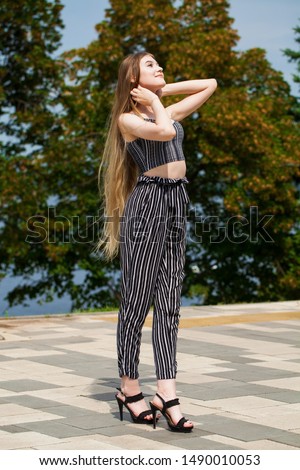 Portrait of a young beautiful girl in striped trousers walks along the promenade