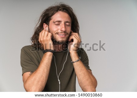 Close up of a smiling young man enjoys listening to music with earphones while standing isolated over gray background