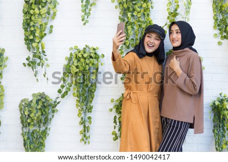Portrait of Two Beautfiul Young Asian Muslim Woman using Smartphone to take a Picture
