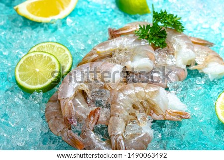 tiger gray green fresh shrimp langoustines with and without a head, lie on the ice blue sea background, slices of lemon and lime are sliced round, around, with greens light, top side view, around