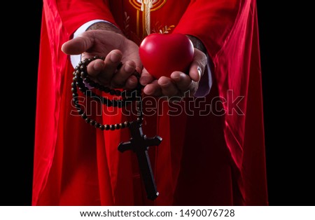 Portrait of pastor  with cross and heart in hands to show love in christian religion with black background