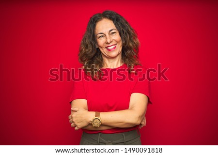 Middle age senior woman with curly hair over red isolated background happy face smiling with crossed arms looking at the camera. Positive person.