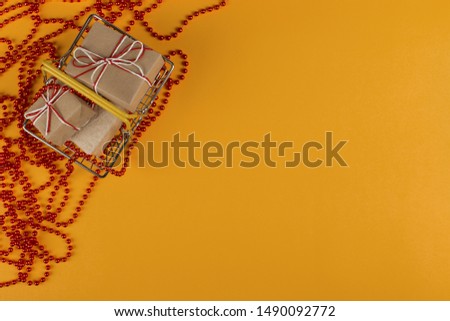 Gifts in a small shopping basket on yellow background with Christmas decorations, concept, copy space.