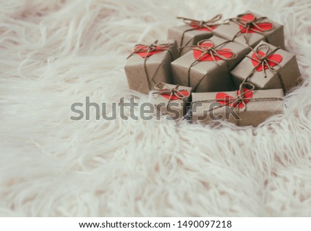 Set of gift boxes wrapped in craft paper and tie hemp string. With cardboard hearts. White fur background.