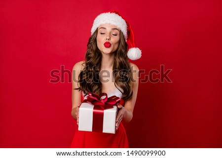 Pretty lady holding big giftbox in hands sending air kiss to handsome santa wear fluffy mini dress isolated red background