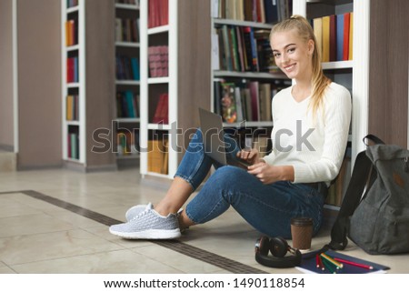 Creative caucasian girl sitting on the floor at library, using laptop, free space