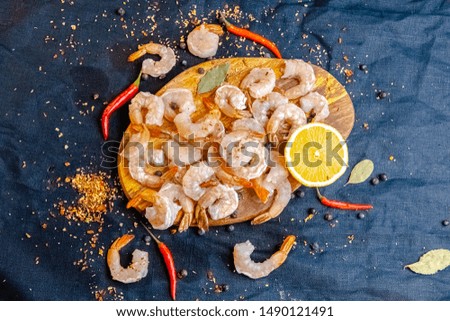 peeled whole red shrimp langoustines, lemon, large sea salt, lying on a dark board around, with greens light, top side view, around