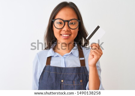 Chinese shopkeeper woman wearing glasses holding credit card over isolated white background with a happy face standing and smiling with a confident smile showing teeth