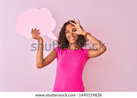 Young brazilian woman holding cloud speech bubble standing over isolated pink background with happy face smiling doing ok sign with hand on eye looking through fingers