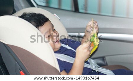 Toddler Asian boy 1.7 year old reading book in child car seat. Entertainment in the car for children concept                              