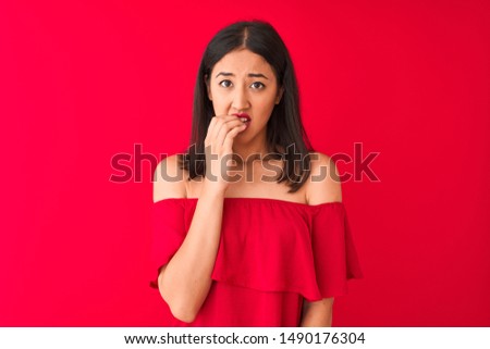 Young beautiful chinese woman wearing casual t-shirt standing over isolated red background looking stressed and nervous with hands on mouth biting nails. Anxiety problem.