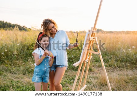 mother teaches daughter paint in park. Sunny nature, mom and daughter paint a picture in a park , painting a Little Child, Child Creativity. Mother's Day