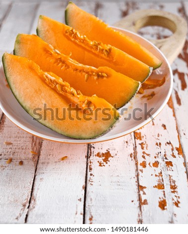 Fresh of sliced orange melon or cantaloupe on wooden cutting board on rustic white wood background.