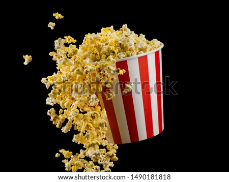 Flying popcorn from paper striped bucket isolated on black background, concept of watching TV or cinema.