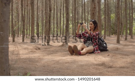 Asian hiker woman trekking in forest. Young happy backpack girl using mobile phone take pictures photo while travel nature and adventure trip, climb mountain in summer holidays vacation concept.