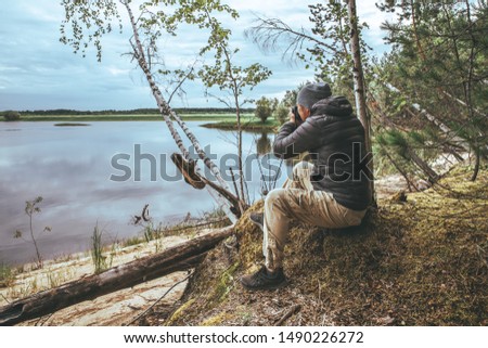 A man with a pick-up in a gray jacket, photographs nature on the banks of the river, in the forest.