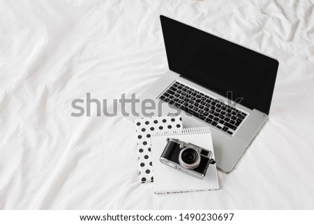 Laptop, notes writing and camera on white bed work at home concept. Top view of a desk working. 