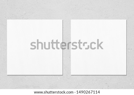 Two empty white square flyer or business card mockups with soft shadows on neutral light grey concrete background. Flat lay, top view