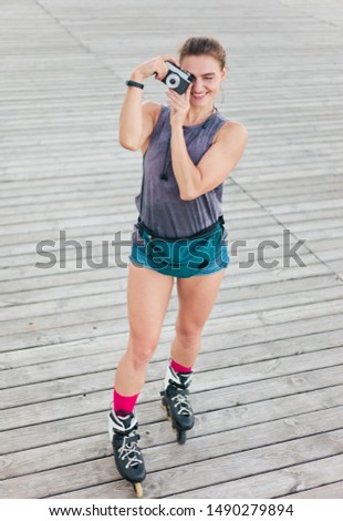 Young attractive sport woman roller skating outdoors and taking pictures on retro camera