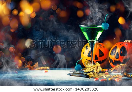 Halloween composition with festive drink, green cocktail and pumpkins lanterns, smoke and fallen leaves on night dark blue background, selective focus