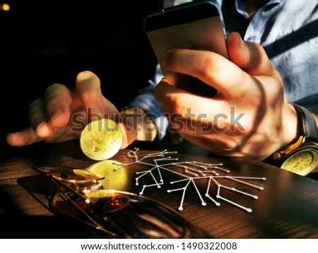 bitcoin holding rich male using his phone for remote exchange e-commerce e-business on the pub table
