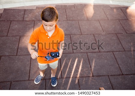 Child learning to pilot a toy helicopter-drone for the first time in the park outside.