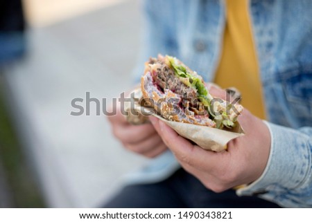 Handsome hipster sitting on street and eating burger close up.
